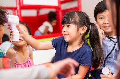 Asian little girl playing as doctor using infrared thermometer check fever temperature measurement of friends in playroom. Preventing Coronavirus concept