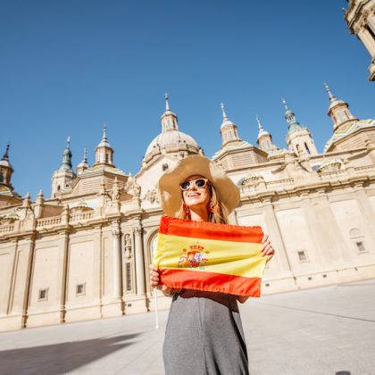 Young woman tourist standing with spanish flag in front of the famous cathedral on the central square during the sunny weather in Zaragoza city, Spain